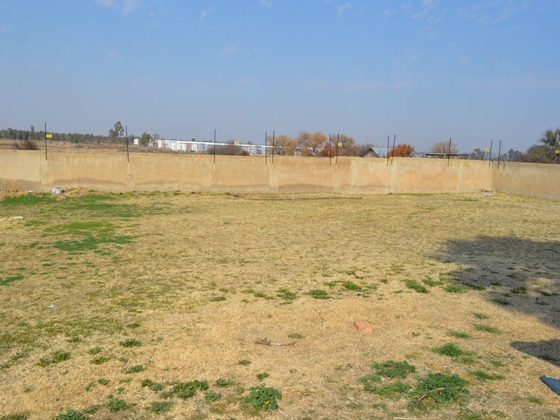 A vacant residential plot featuring a perimeter wall with installed electric fencing and an open grassed area.