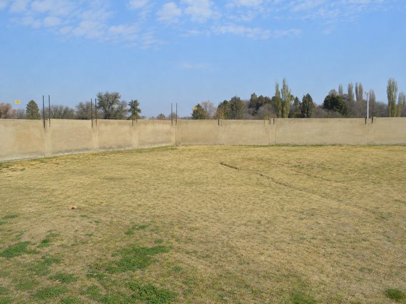 A vacant residential plot featuring a level grass area enclosed by a perimeter wall with installed electric fencing.