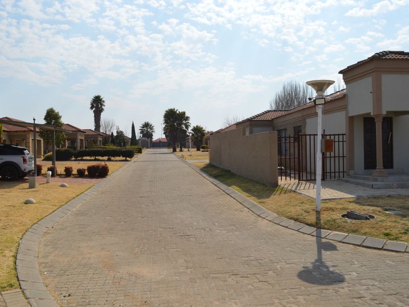 A view of a paved residential street within a housing estate, featuring well-maintained boundary walls, driveways, and established landscaping.