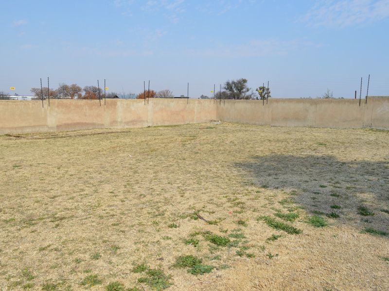 A vacant residential plot featuring a level grassed area enclosed by a perimeter wall with installed electric fencing.