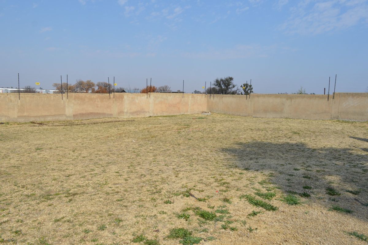 A vacant residential plot featuring a perimeter wall with installed electric fencing and dry grass coverage.