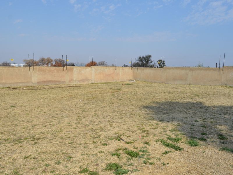 A vacant residential plot featuring a perimeter wall with installed electric fencing and dry grass coverage.