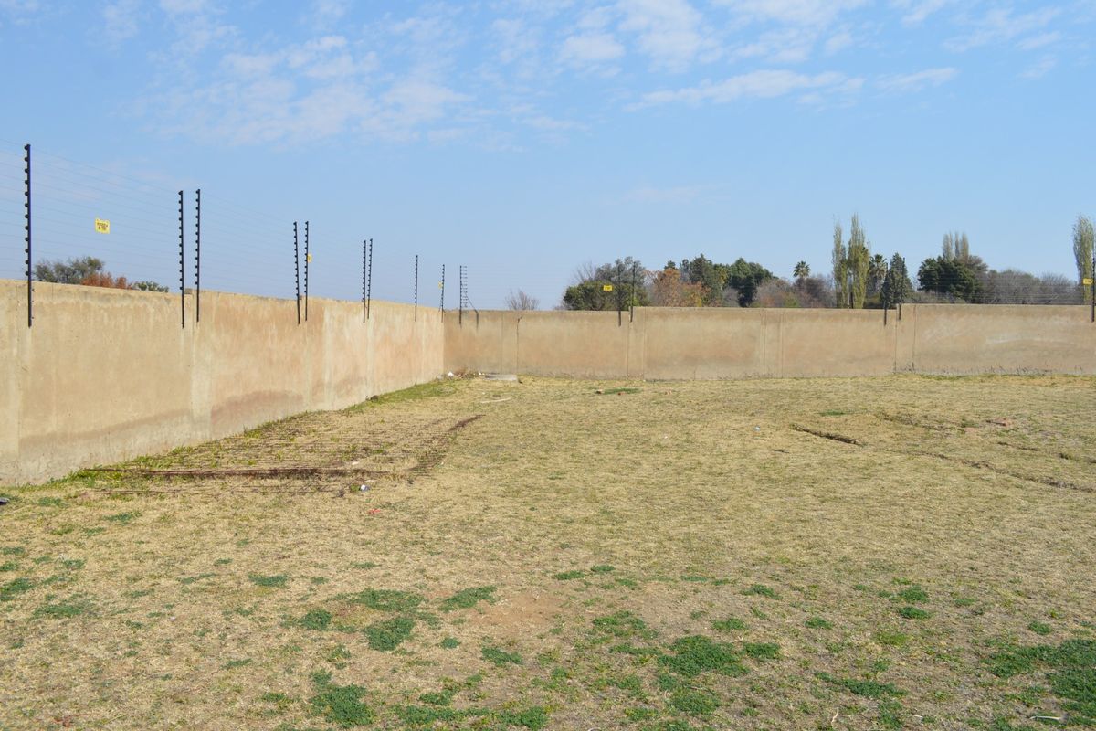 A vacant residential plot featuring a perimeter wall with installed electric fencing, offering a clear space for future development.