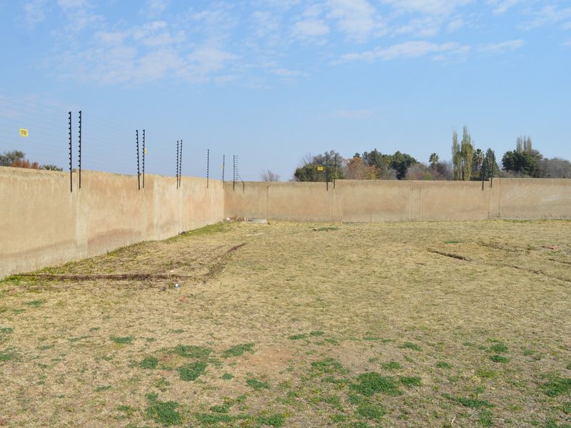 A vacant residential plot featuring a perimeter wall with installed electric fencing, offering a clear space for future development.