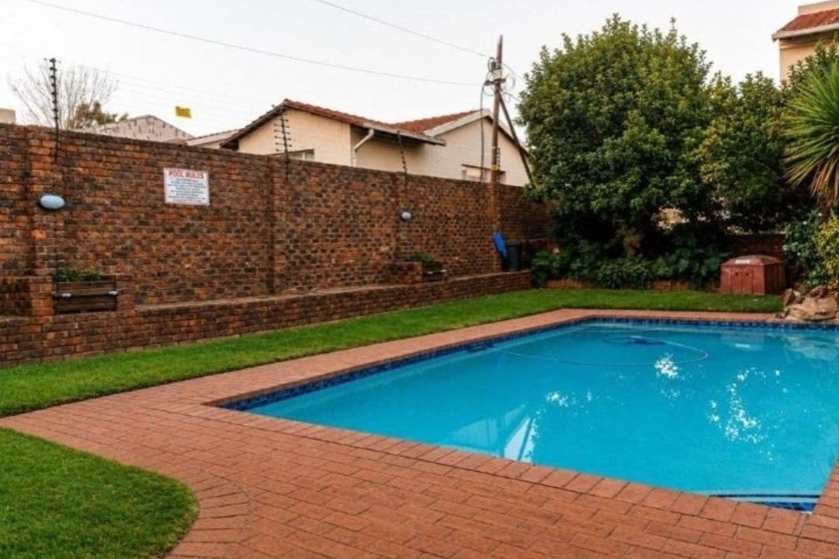 A well-maintained outdoor pool area featuring a clear swimming pool, brick paving, and a secure brick boundary wall with electric fencing.