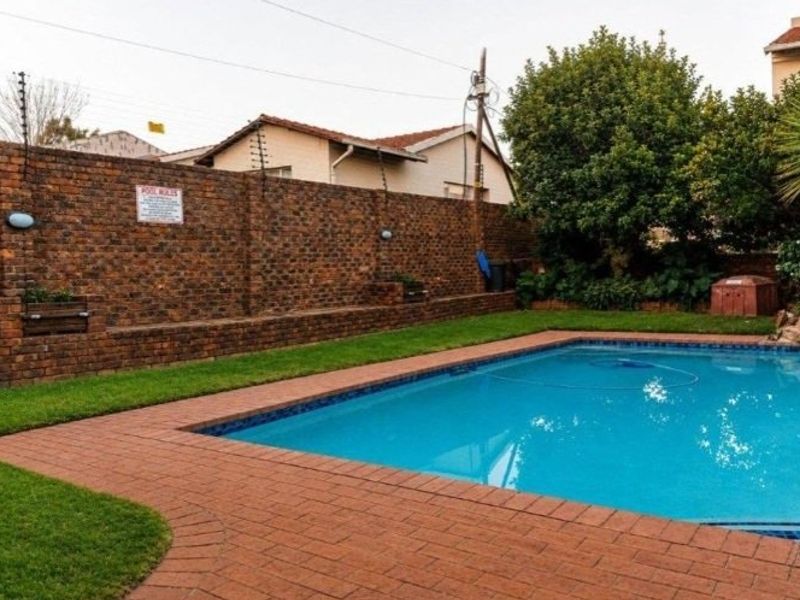 A well-maintained outdoor pool area featuring a clear swimming pool, brick paving, and a secure brick boundary wall with electric fencing.