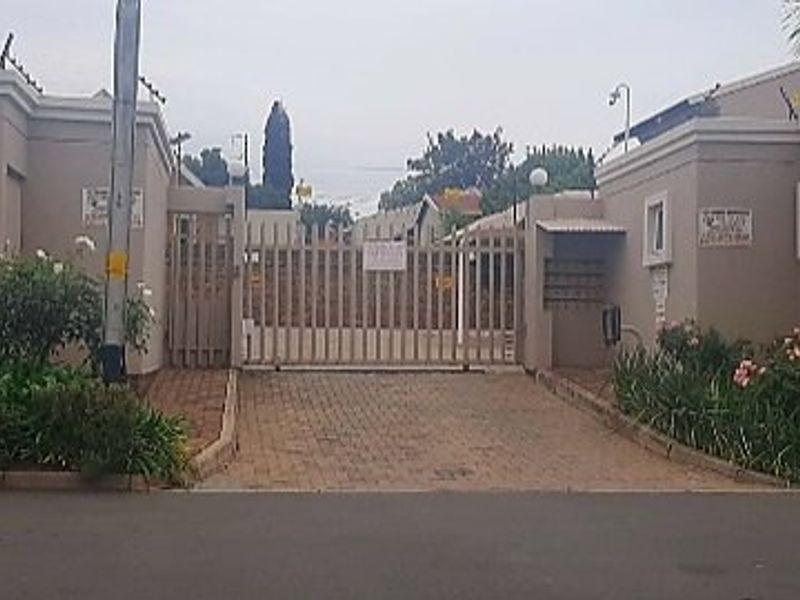 Front entrance view of the apartment complex featuring a secure gated access point, paved driveway, and perimeter wall with electric fencing.