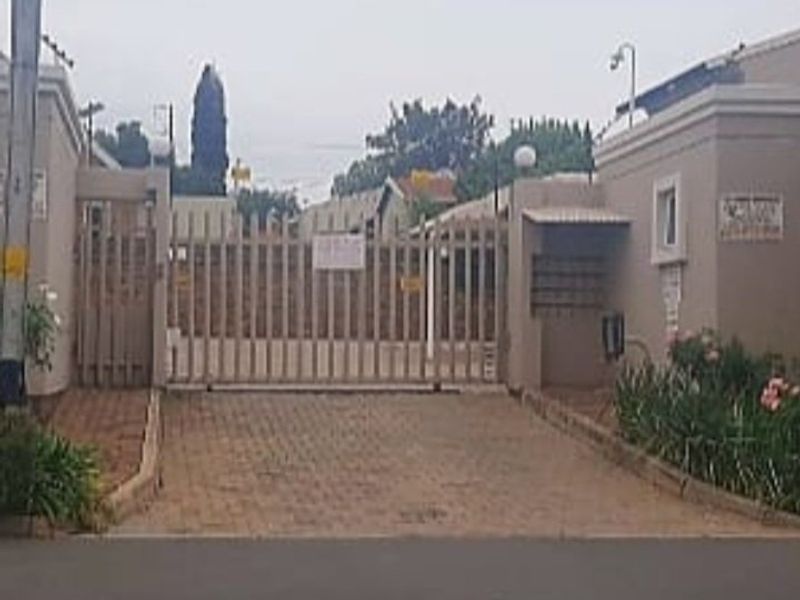The entrance to the apartment complex features a secure gated access point with a paved driveway and integrated post boxes.