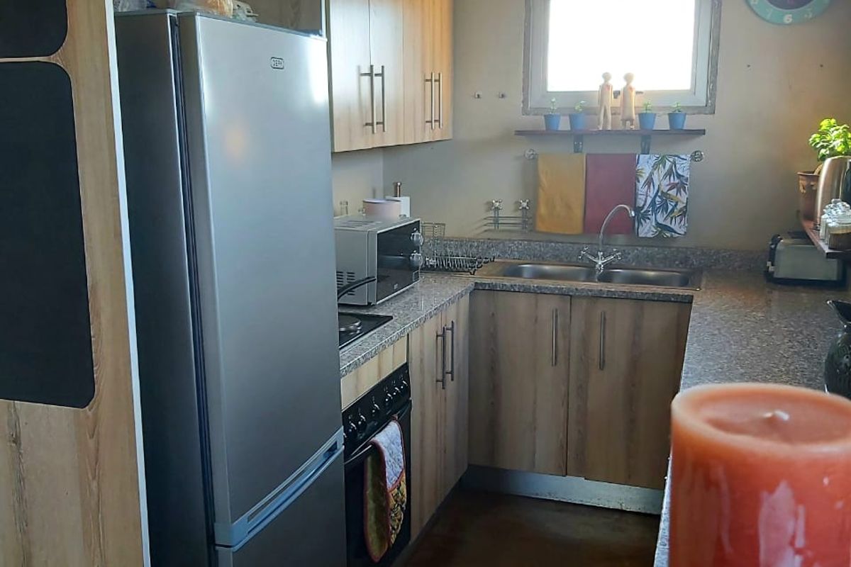 Compact kitchen featuring wood-look laminate cabinetry, granite countertops, a double basin sink, and integrated oven and hob.