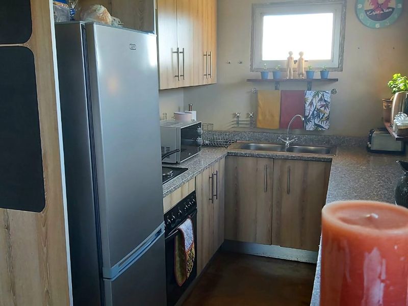 Compact kitchen featuring wood-look laminate cabinetry, granite countertops, a double basin sink, and integrated oven and hob.