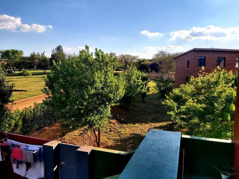 An elevated view overlooking the surrounding estate grounds, featuring mature trees, landscaped garden areas, and neighboring residential buildings.