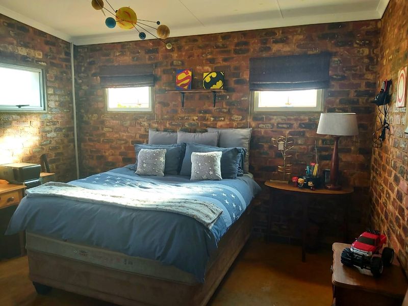 A bedroom featuring rustic exposed brick walls, multiple casement windows with roller blinds, and a warm, textured aesthetic.