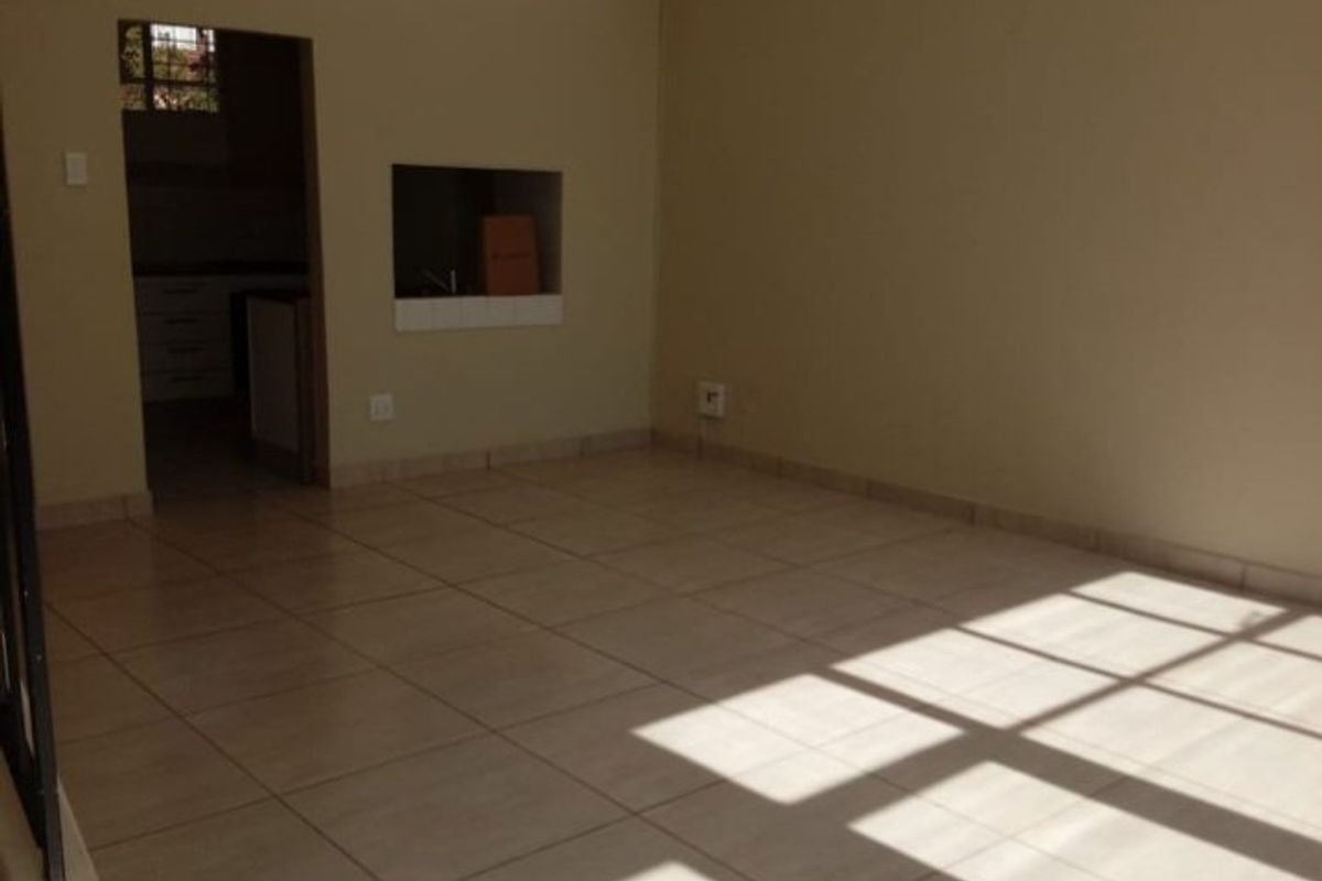 An empty, sunlit living area featuring neutral tiled flooring and a convenient pass-through window connecting to the adjacent kitchen space.