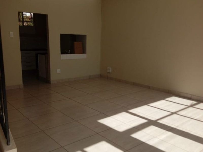 An empty, sunlit living area featuring neutral tiled flooring and a convenient pass-through window connecting to the adjacent kitchen space.