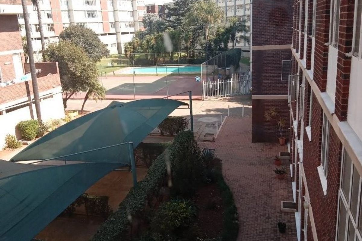 An elevated view of the townhouse complex grounds featuring brick pathways, a communal swimming pool, and shaded parking areas.