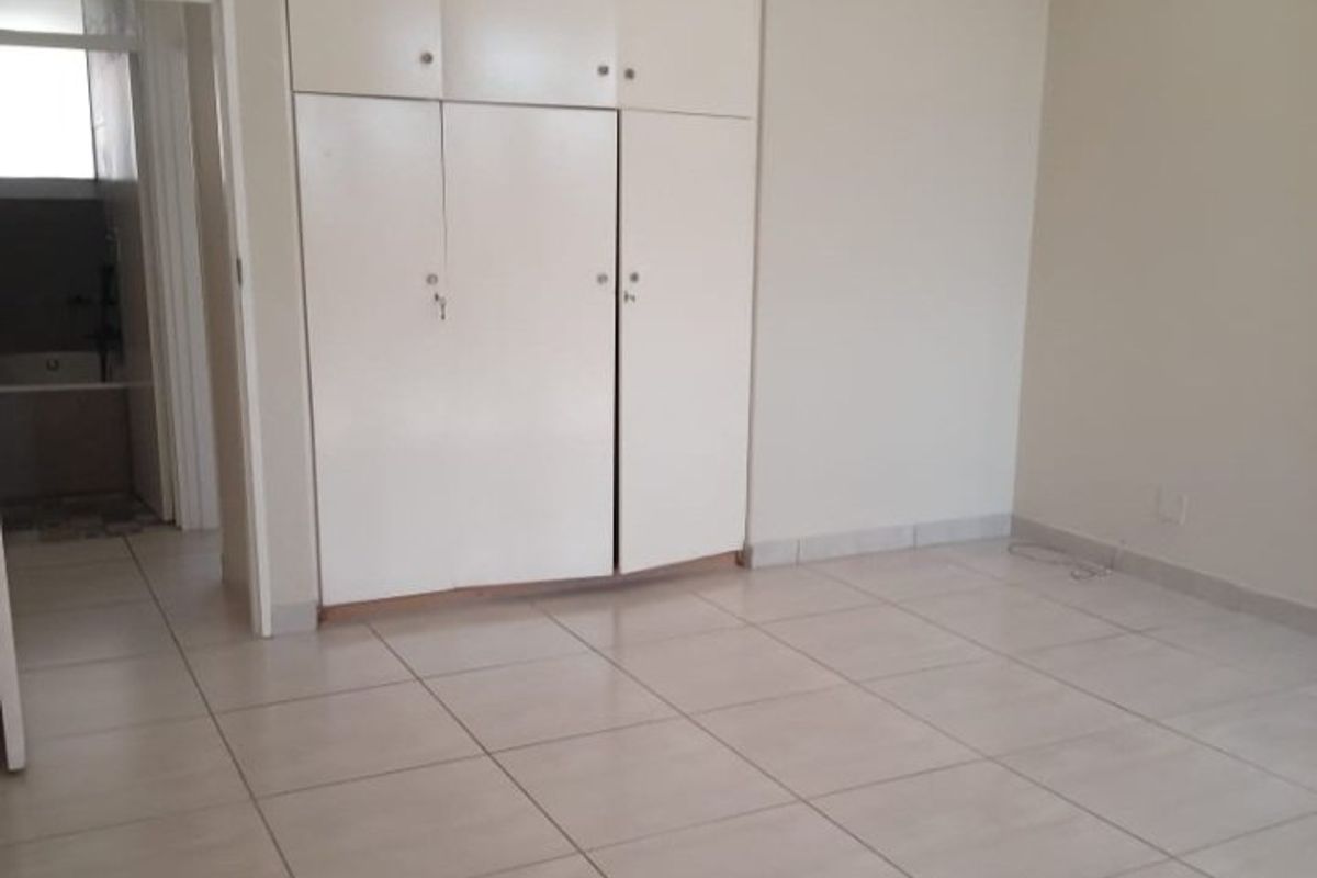 A bright, empty bedroom featuring neutral tiled flooring and ample built-in cupboard storage, offering a clean and versatile space.