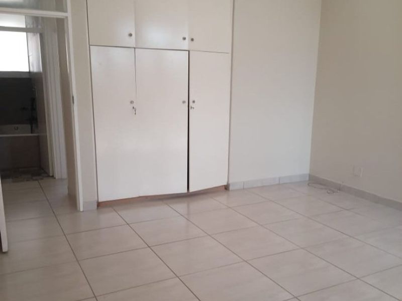 A bright, empty bedroom featuring neutral tiled flooring and ample built-in cupboard storage, offering a clean and versatile space.