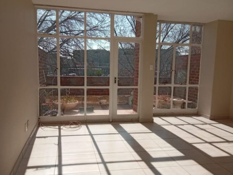An empty, sunlit living area featuring large glass windows and doors that provide access to an outdoor patio space.