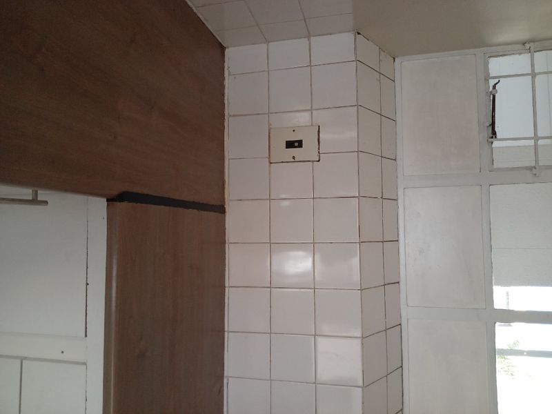 A close-up view of a kitchen corner featuring dated wall tiles, built-in cabinetry, and a security window gate.