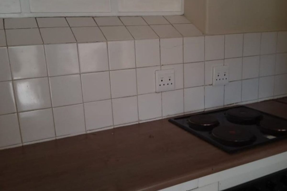 A functional kitchen area featuring a built-in oven, electric hob, laminate countertops, and a tiled backsplash with integrated power outlets.