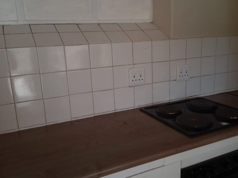 A functional kitchen area featuring a built-in oven, electric hob, laminate countertops, and a tiled backsplash with integrated power outlets.