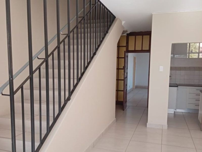 A bright, tiled hallway featuring a metal staircase railing, leading into an open-plan kitchen area with built-in cabinetry.