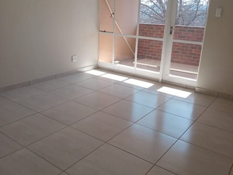 An empty living room featuring neutral tiled flooring and a large glass door providing access to an outdoor balcony area.