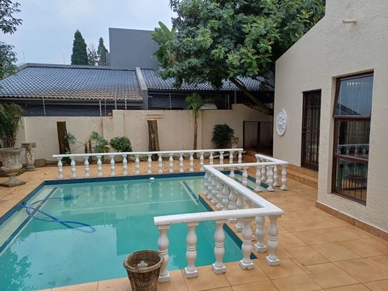 Outdoor pool area featuring a tiled patio, decorative balustrade, and perimeter boundary wall, providing a private space for relaxation and entertainment.
