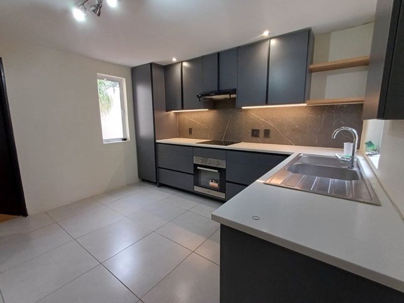 Modern kitchen featuring dark grey cabinetry, stone countertops, integrated appliances, and sleek tiled flooring with under-cabinet lighting.