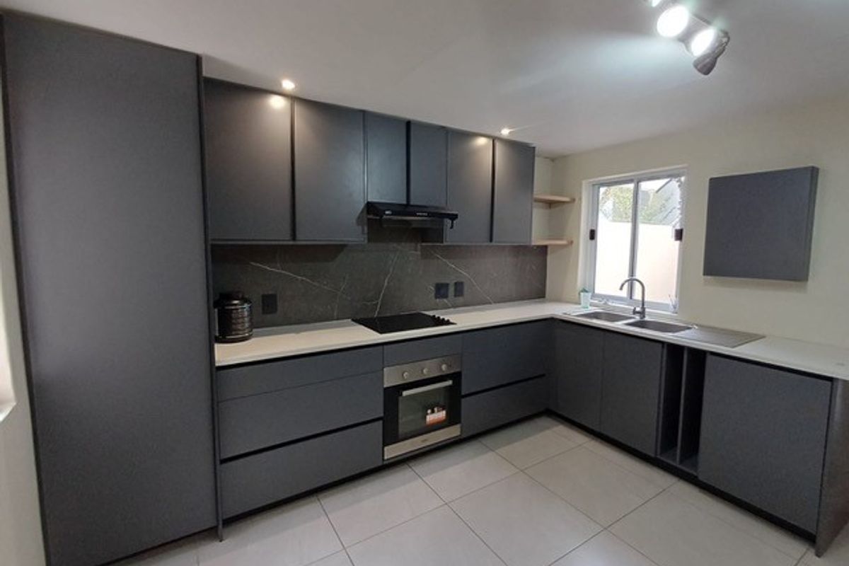 Modern kitchen featuring dark grey cabinetry, stone countertops, integrated oven, electric hob, and tiled flooring in a clean, contemporary layout.