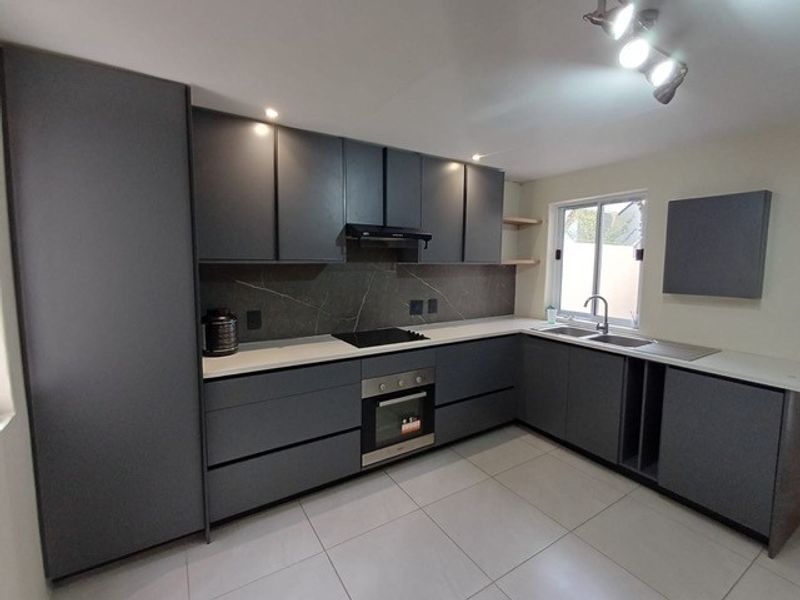 Modern kitchen featuring dark grey cabinetry, stone countertops, integrated oven, electric hob, and tiled flooring in a clean, contemporary layout.