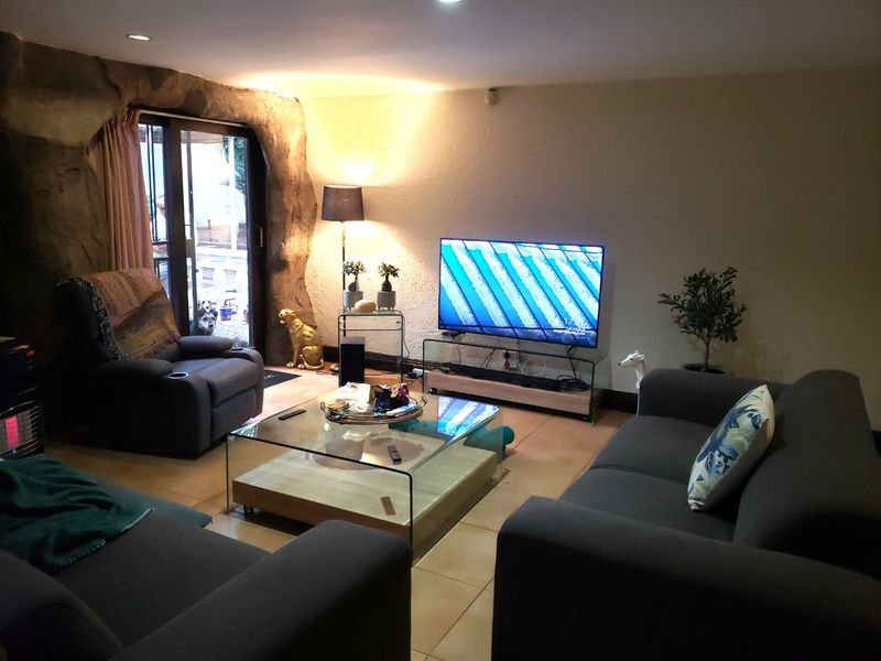 A cozy living room featuring tiled flooring, recessed lighting, and a unique decorative rock-effect wall surrounding the sliding glass door access to the exterior.