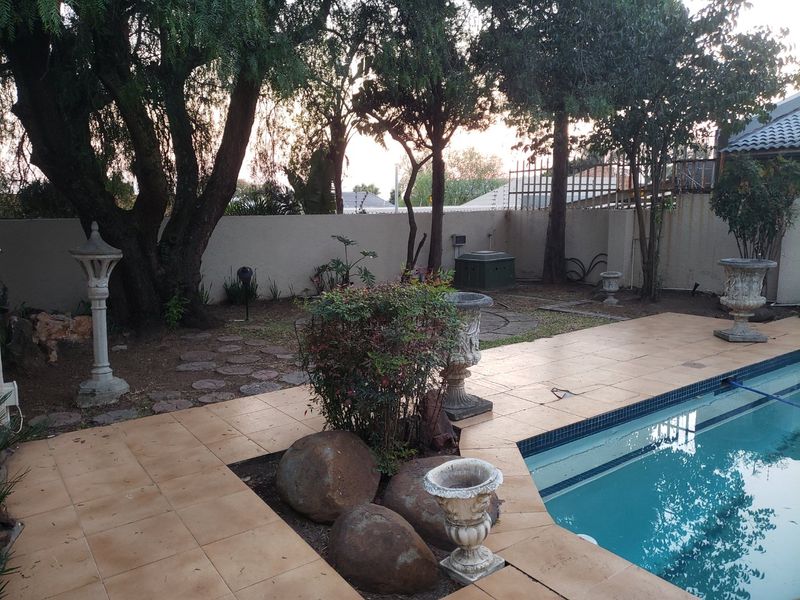 Outdoor pool area featuring a tiled surround, perimeter wall, and established trees, providing a private space for relaxation and recreation.