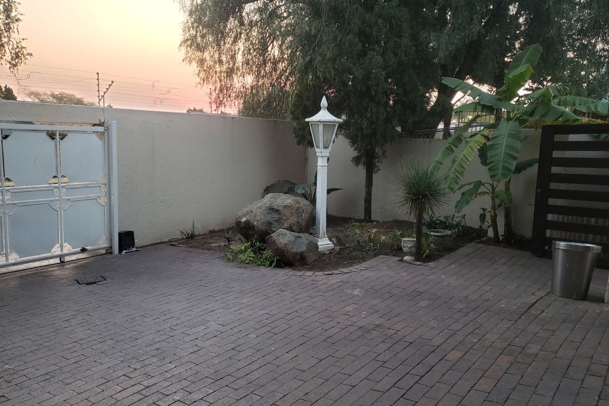 A paved rear courtyard area featuring a boundary wall, decorative lamp post, and established garden elements.