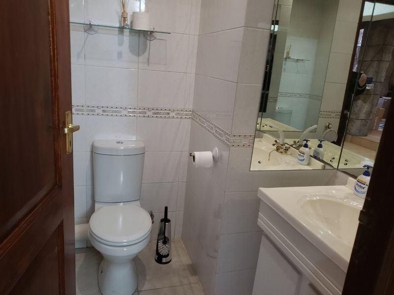 A functional bathroom featuring a white toilet, vanity basin with integrated mirror, and neutral wall tiling.