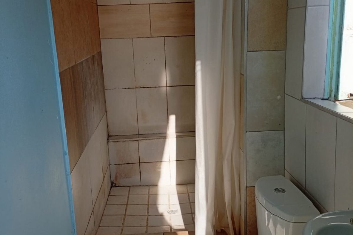 A functional bathroom featuring a shower cubicle, toilet, and washbasin with dated wall and floor tiling.