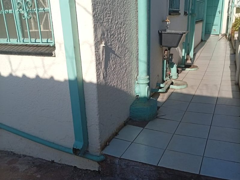 Side exterior walkway featuring tiled flooring, security bars on windows, and an external utility sink with plumbing fixtures.