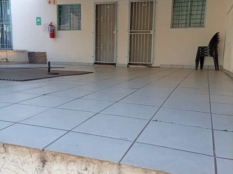 A covered outdoor patio area featuring tiled flooring, security gates, and a corrugated metal roof, showing signs of wear on the exterior base.