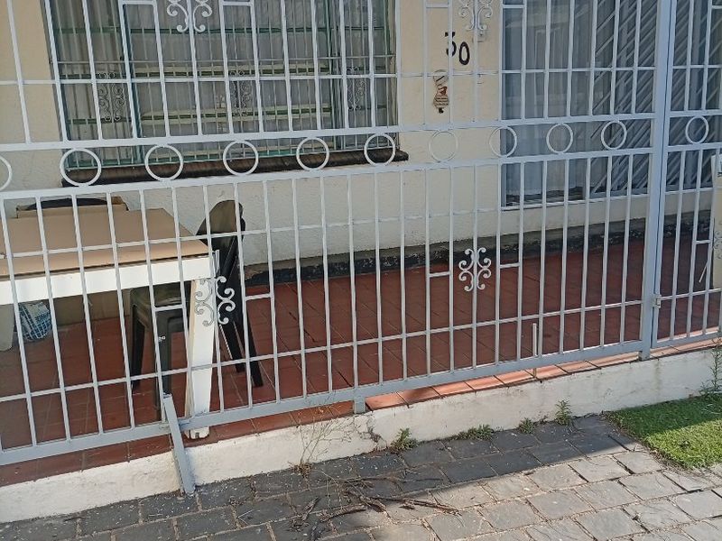 Front exterior view of the property featuring a paved driveway, a tiled patio area, and a full-height security gate.
