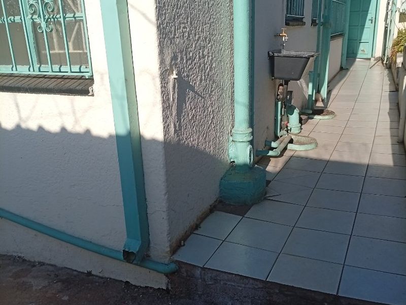 Side exterior walkway featuring tiled flooring, security bars on windows, and an external utility sink with plumbing fixtures.