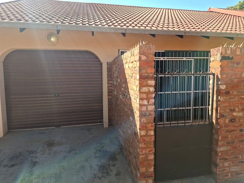 Front exterior view of the townhouse featuring a roll-up garage door, brick boundary wall with security spikes, and a metal security gate.