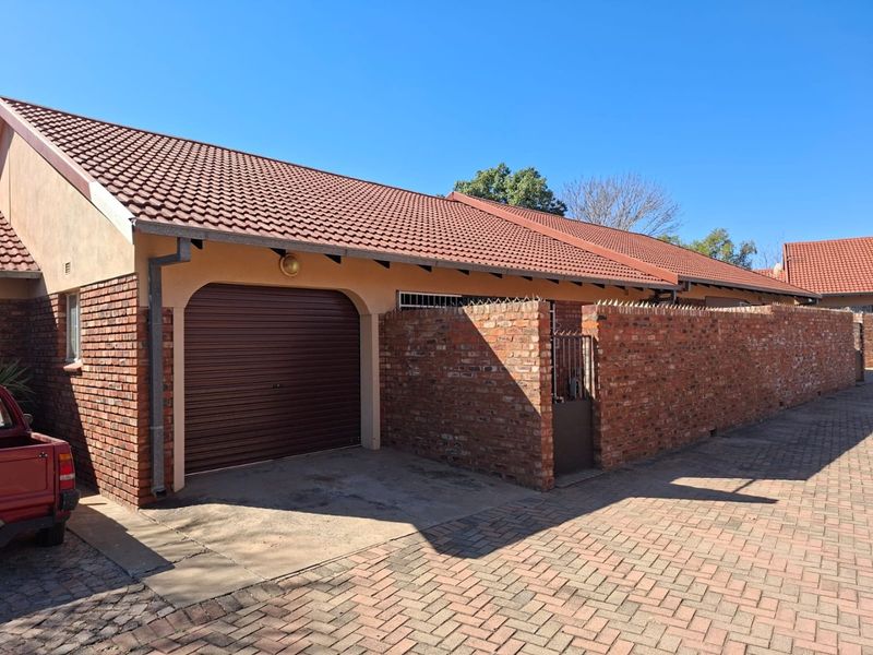 Front exterior view of a townhouse featuring a brick facade, tiled roof, single roll-up garage, and a paved driveway with perimeter walling.