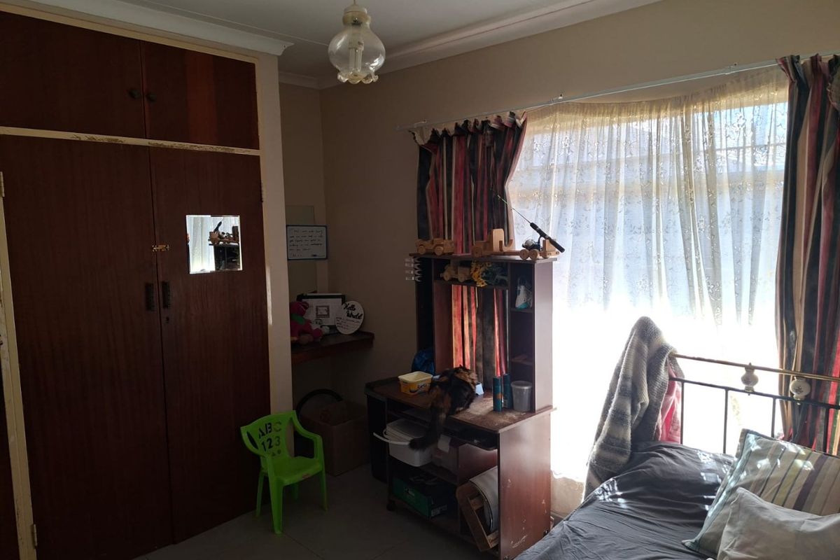 A bedroom featuring tiled flooring and a built-in wooden wardrobe with visible wear, offering a functional space with natural light.