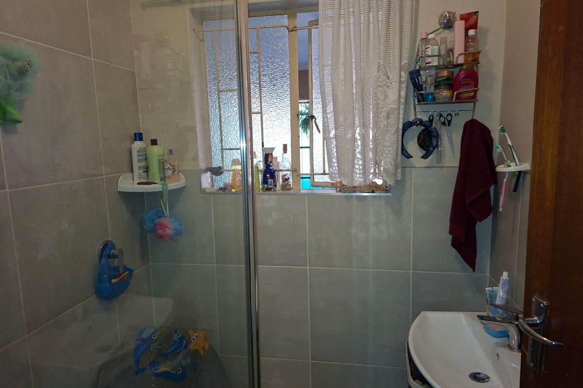 A functional bathroom featuring a glass-enclosed shower, ceramic wall tiling, and a pedestal washbasin with a window providing natural light.