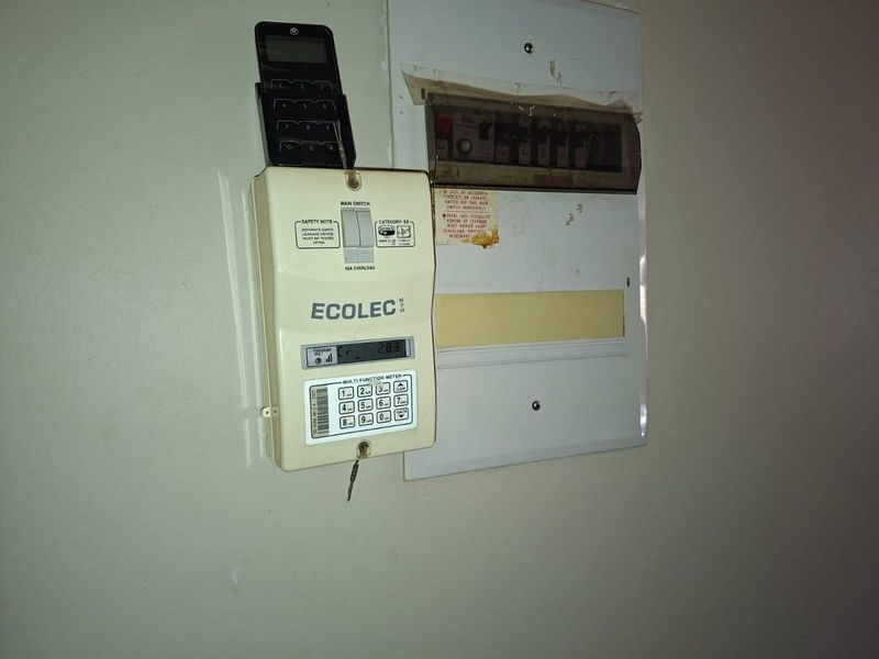 A wall-mounted prepaid electricity meter and electrical distribution board with visible wear on the protective covers.