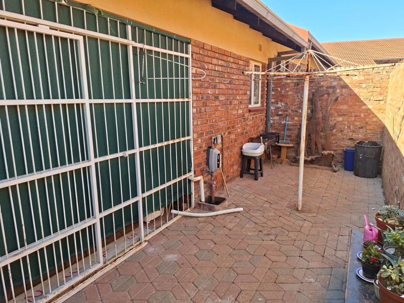 A paved rear courtyard area featuring exposed brick walls, a security gate, and a fixed washing line, offering a functional outdoor utility space.