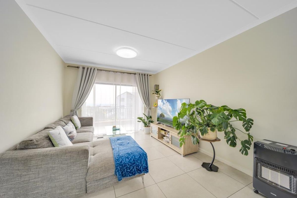 A bright and well-maintained living room featuring large format floor tiles and a sliding glass door providing access to the balcony.