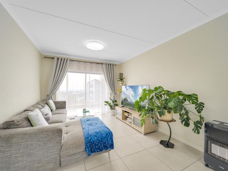 A bright and well-maintained living room featuring large format floor tiles and a sliding glass door providing access to the balcony.