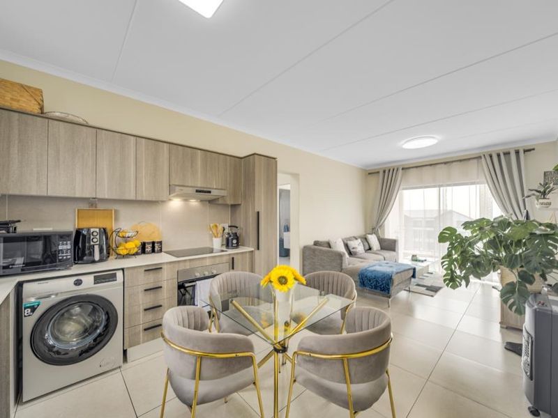 Modern open-plan living area featuring a contemporary kitchen with built-in cabinetry, integrated appliances, and tiled flooring, leading to a bright lounge with balcony access.
