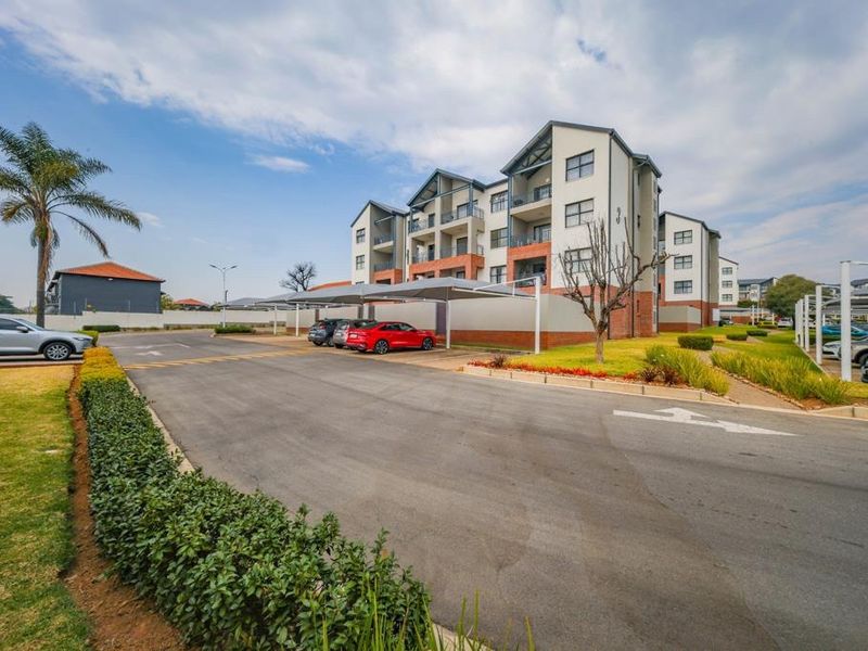 Exterior view of a modern apartment complex featuring paved driveways, covered parking bays, and landscaped grounds.
